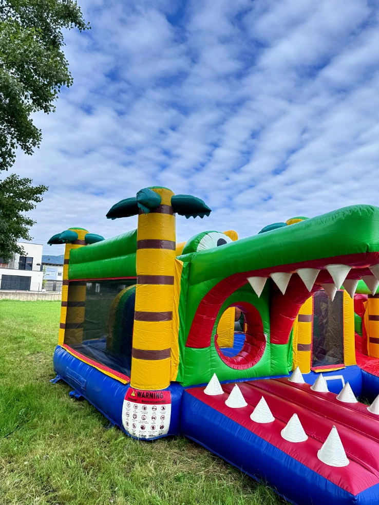 Napihljivo igralo v obliki zelenega krokodila z odprtimi čeljustmi – atrakcija za zabavne otroške dogodke na prostem.